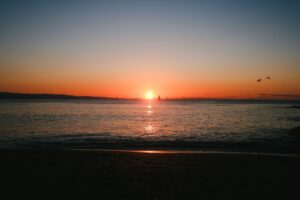 the sun is setting over the water at the beach